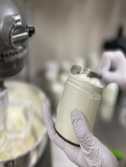Person holding a container of cream in a kitchen setting with a mixer in the background