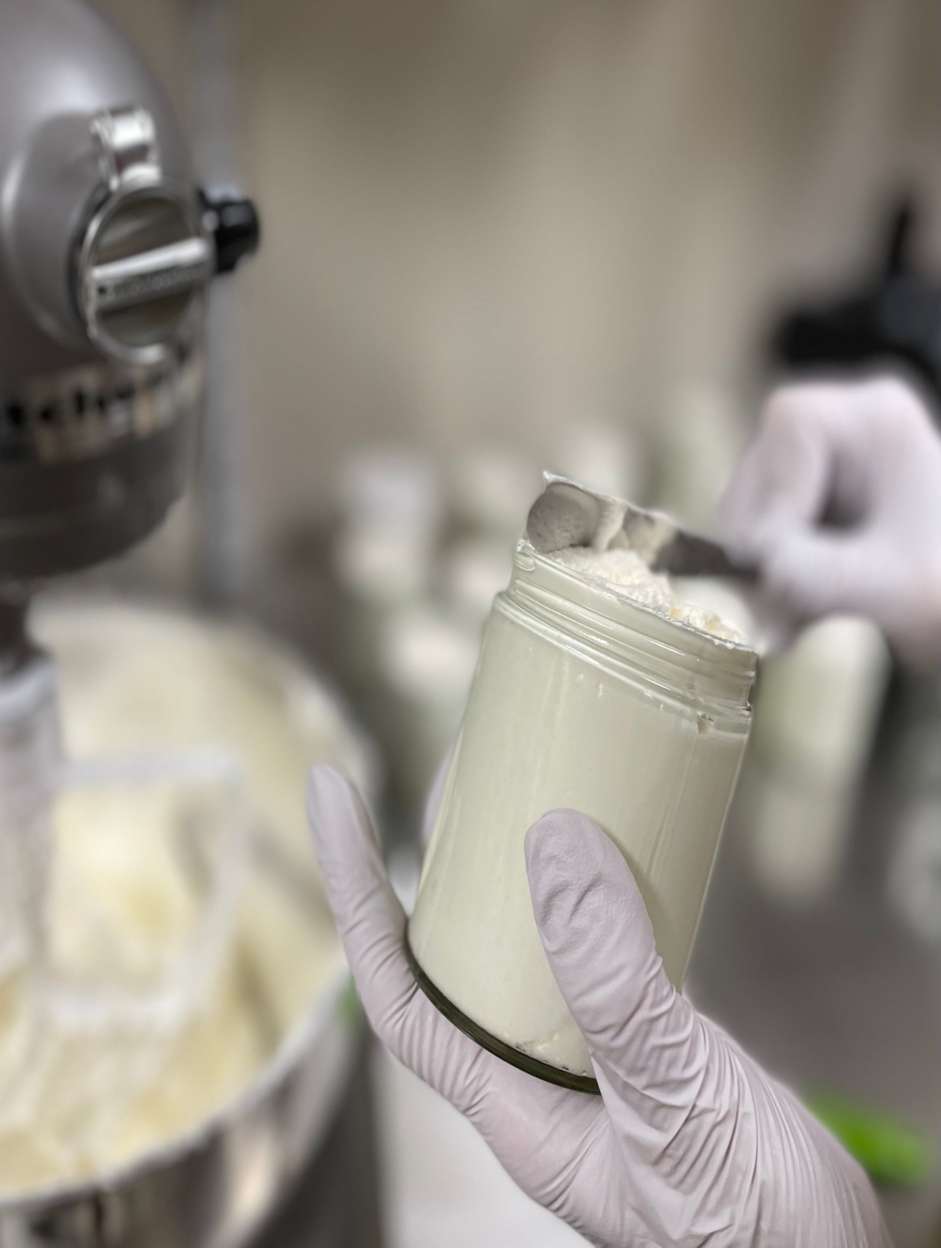 Person holding a container of cream in a kitchen setting with a mixer in the background