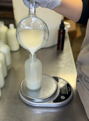 Person measuring liquid in a glass container on a digital scale in a laboratory setting.