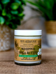 Jar of Mion Artisan Soap whipped shea butter on a wooden surface with a blurred background