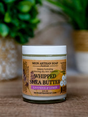 Jar of Mion Artisan Soap whipped shea butter with a blurred green plant in the background