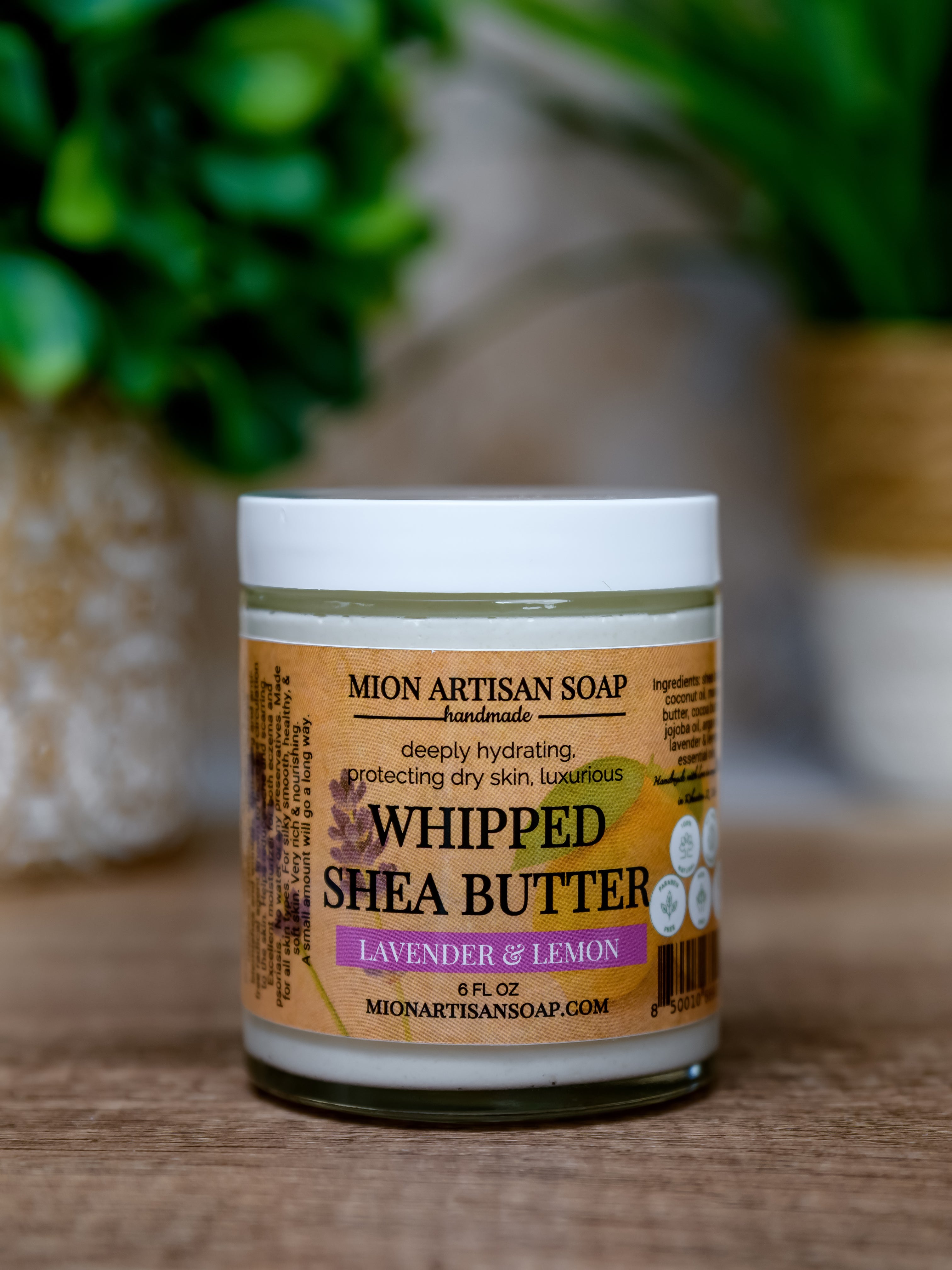 Jar of Mion Artisan Soap whipped shea butter with a blurred green plant in the background