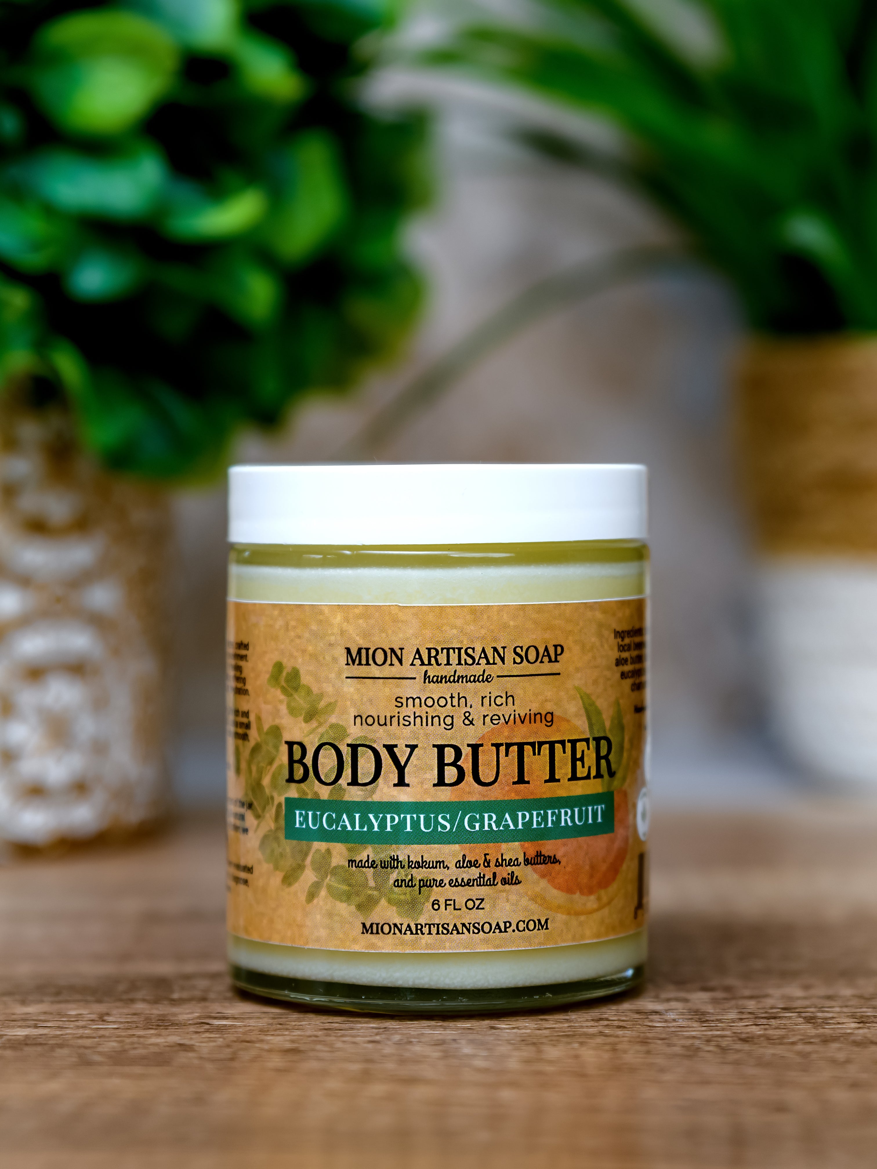 Jar of Mion Artisan Soap body butter on a wooden surface with plants in the background