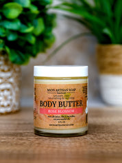 Jar of Mion Artisan Soap Body Butter with a rose blossom scent on a wooden surface.
