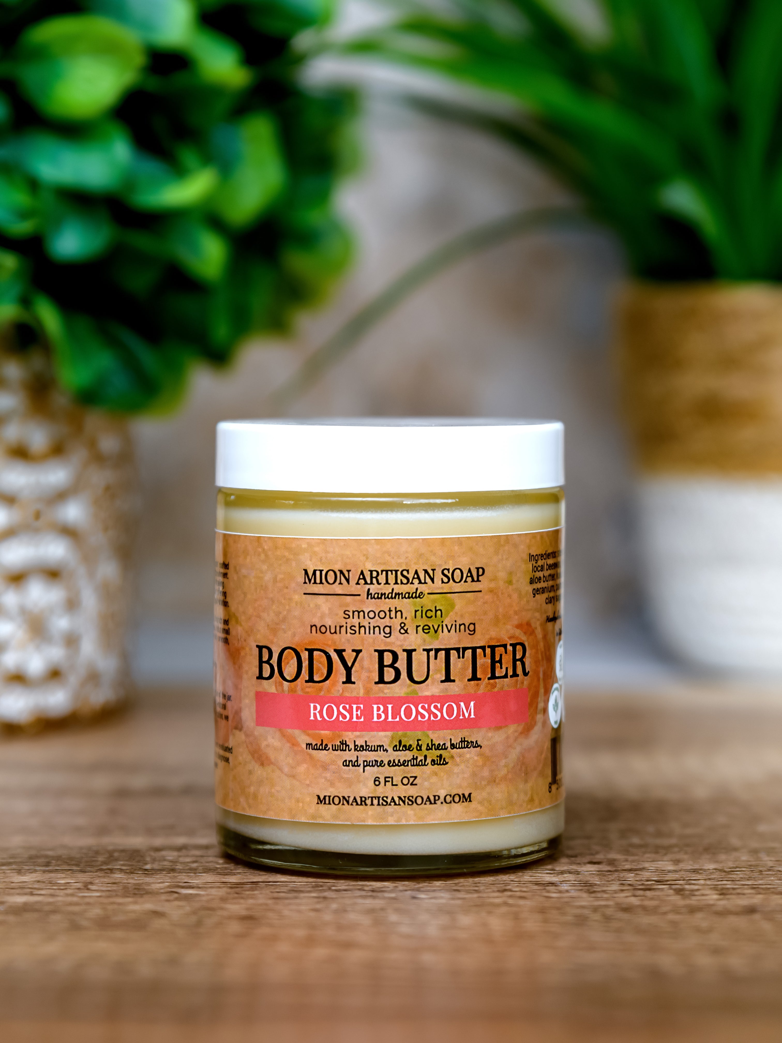Jar of Mion Artisan Soap Body Butter with a rose blossom scent on a wooden surface.