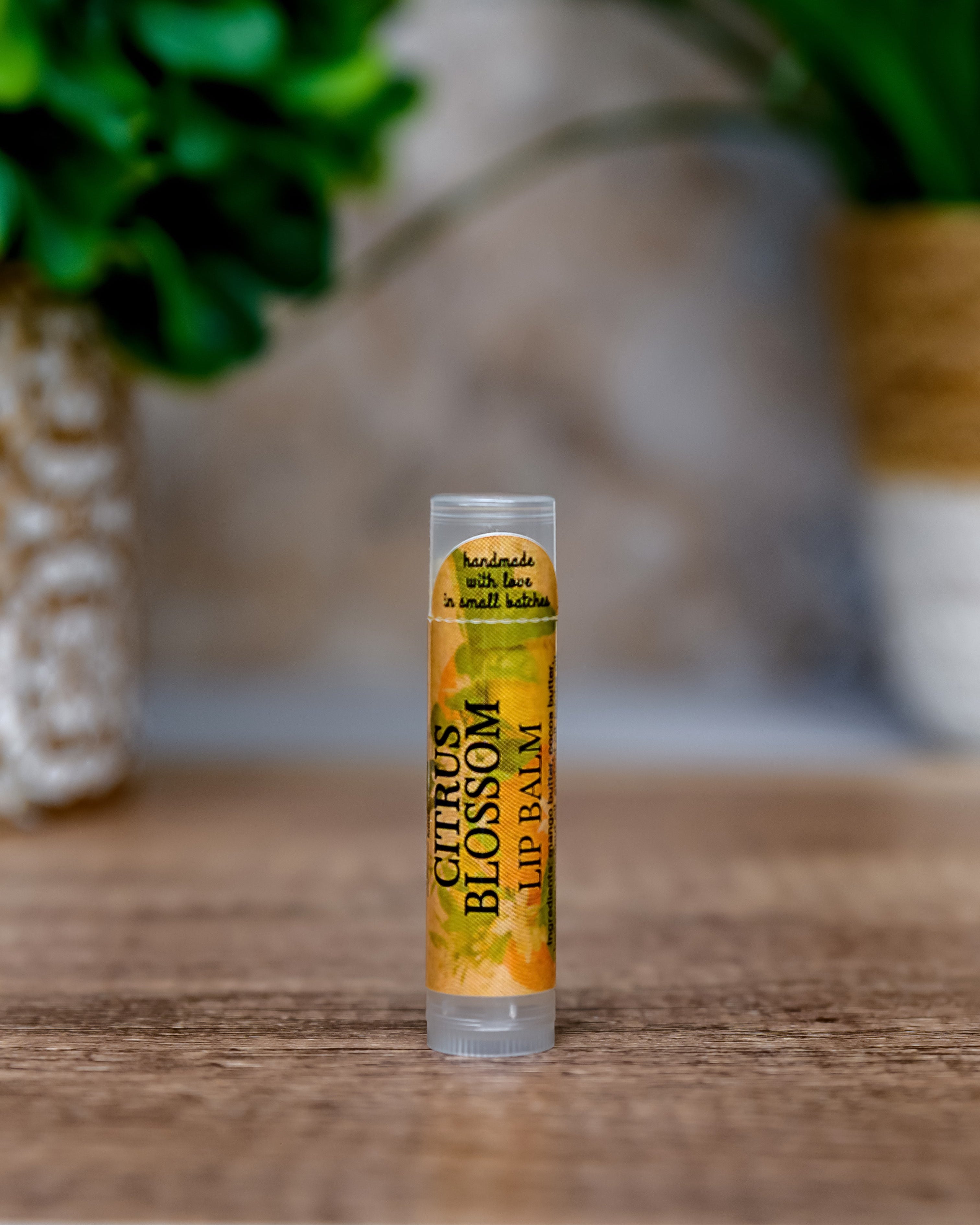 Lip balm tube labeled 'Citrus Blossom' on a wooden surface with a blurred natural background