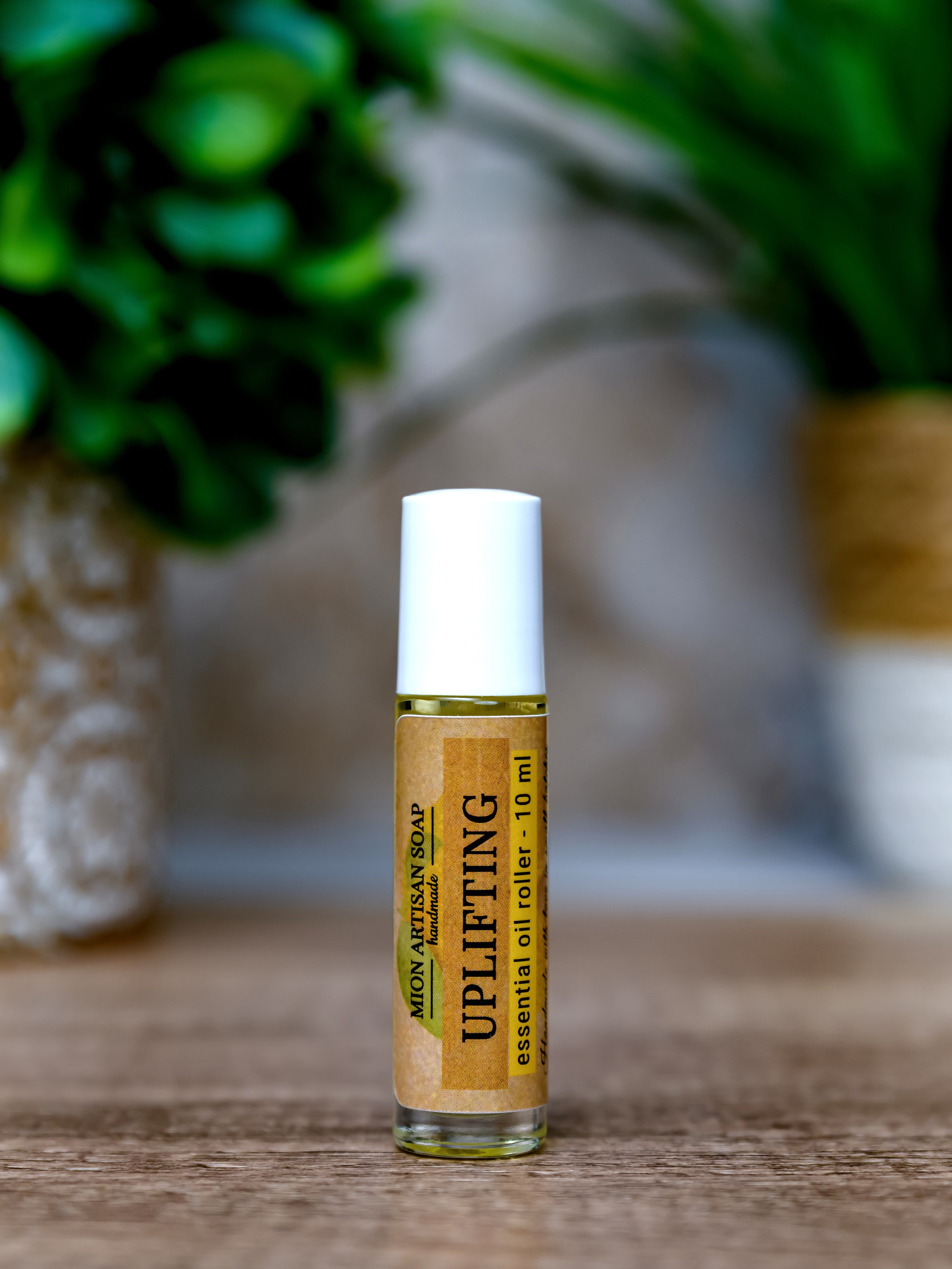 Roll-on bottle of essential oil labeled 'Uplifting' on a wooden surface with a blurred natural background.
