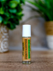 Roll-on bottle labeled 'Energy Alertness' on a wooden surface with a blurred green plant in the background.