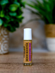 Roll-on bottle labeled 'Mood Booster' on a wooden surface with a blurred green plant in the background.