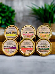 Set of six hand balm containers with various scents on a wooden surface.