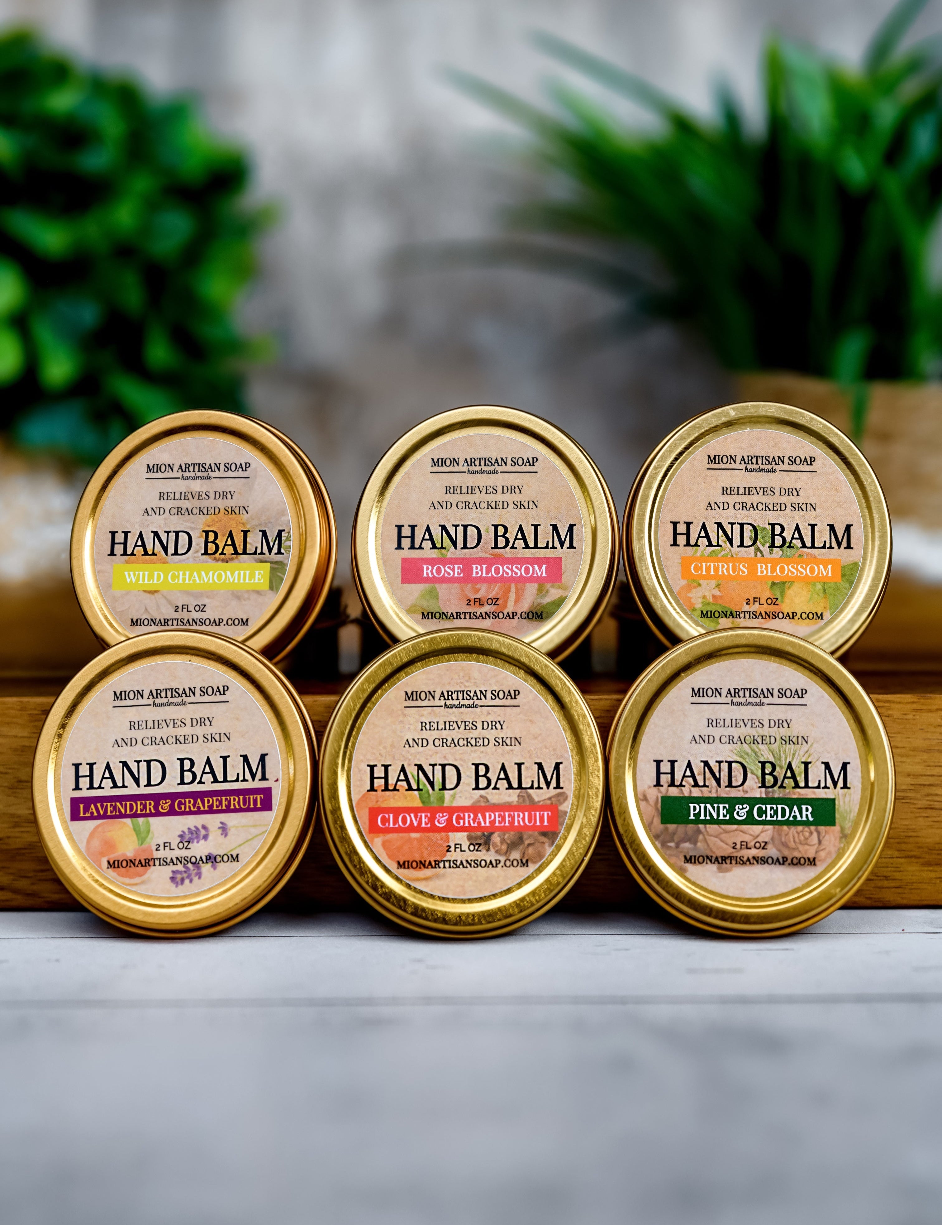 Set of six hand balm containers with various scents on a wooden surface.