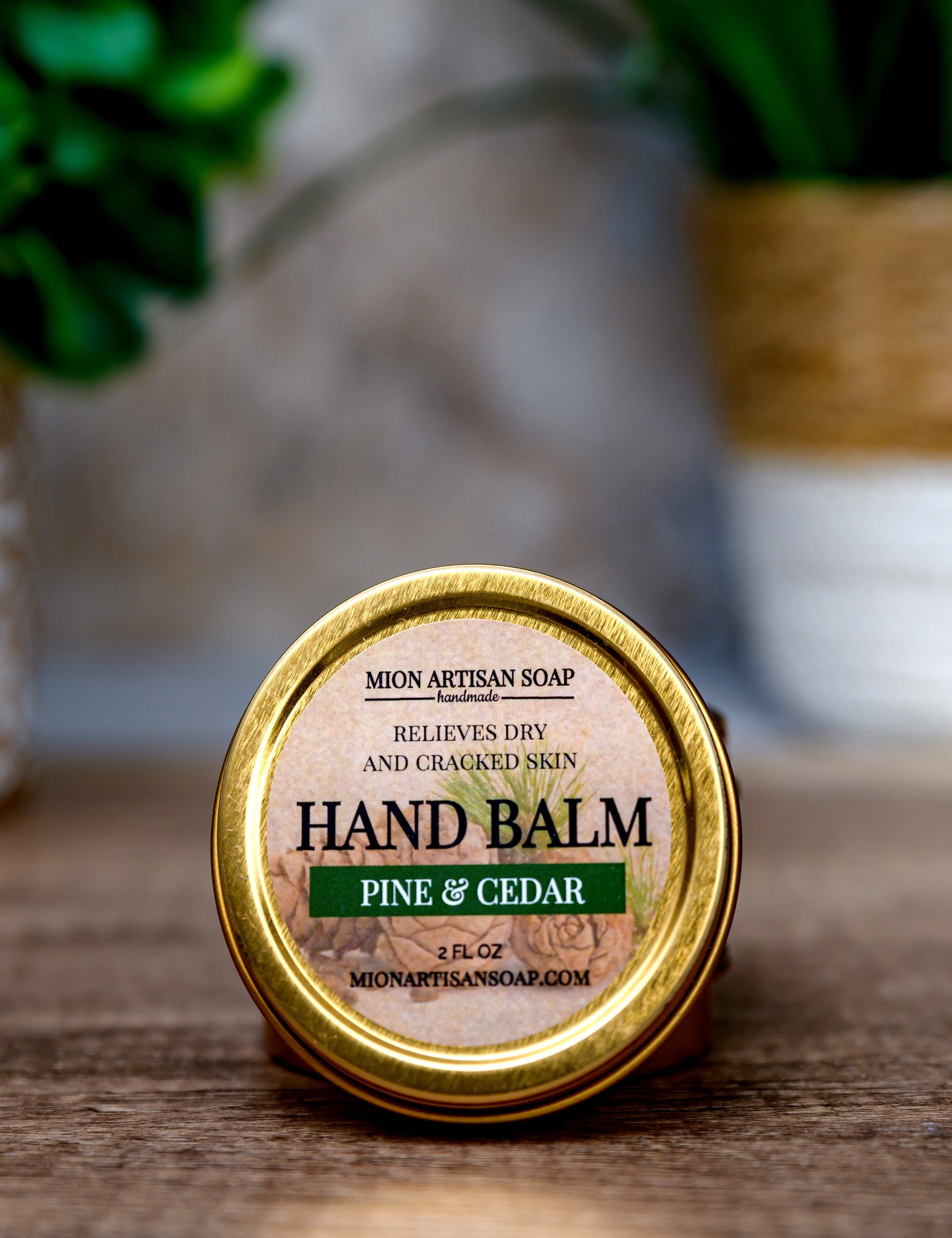 Hand balm container labeled 'Pine & Cedar' on a wooden surface with a blurred natural background.