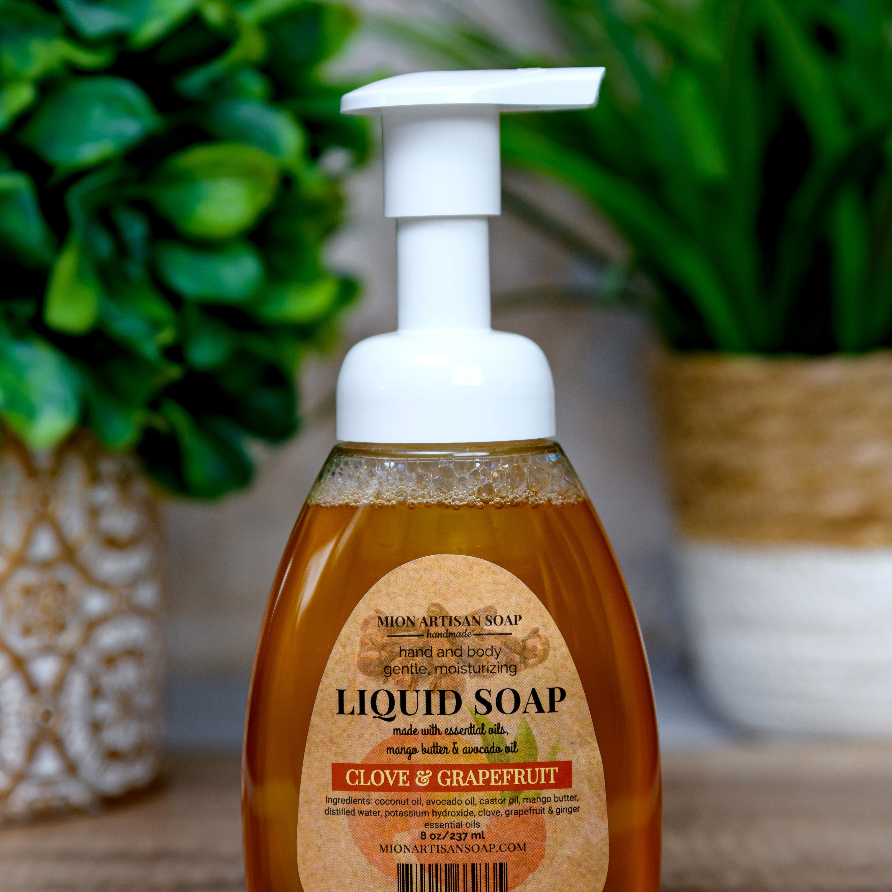 Bottle of liquid soap with a label on a wooden surface with plants in the background