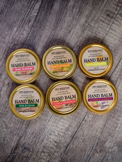 Six tins of hand balm with gold lids on a wooden surface