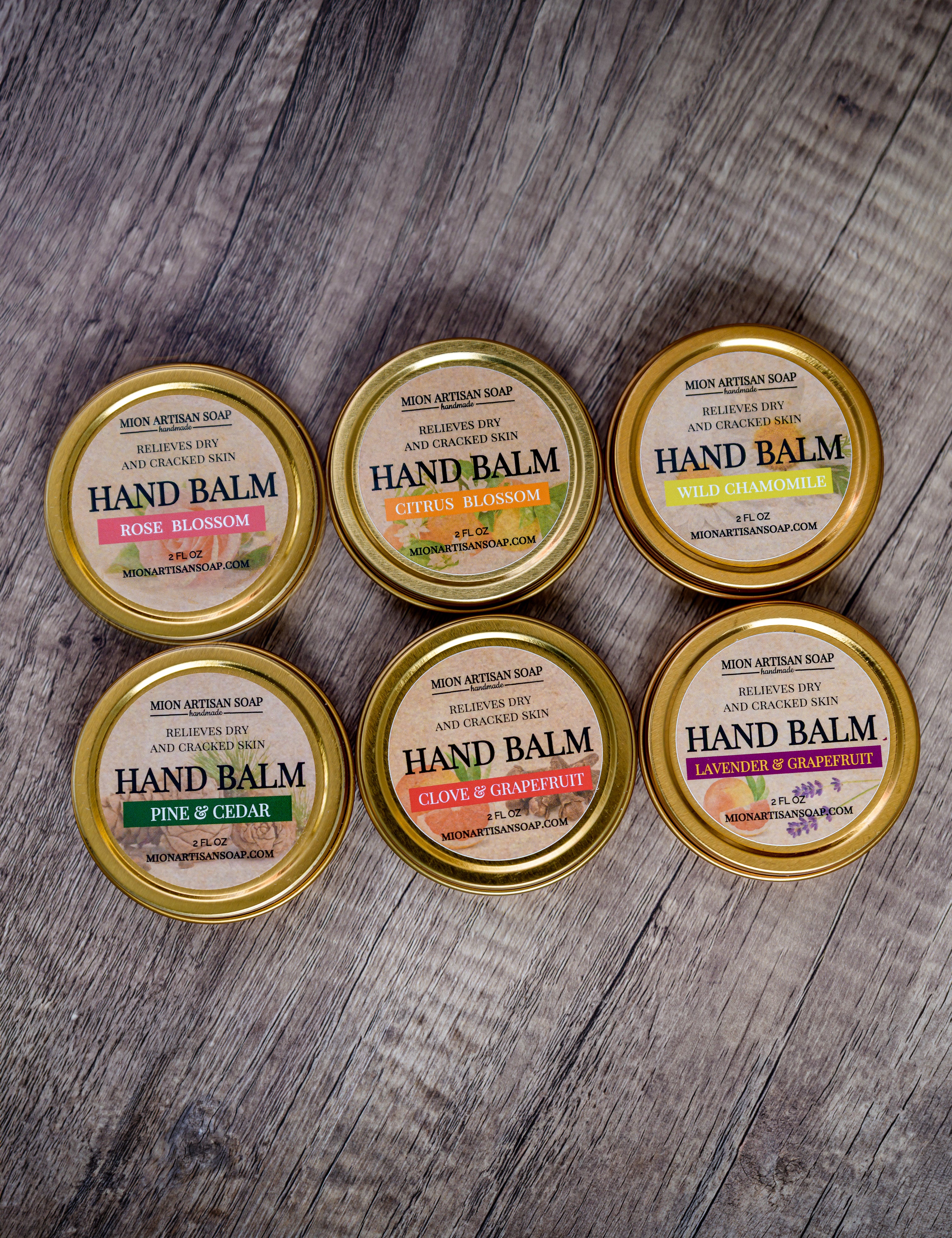 Six tins of hand balm with gold lids on a wooden surface