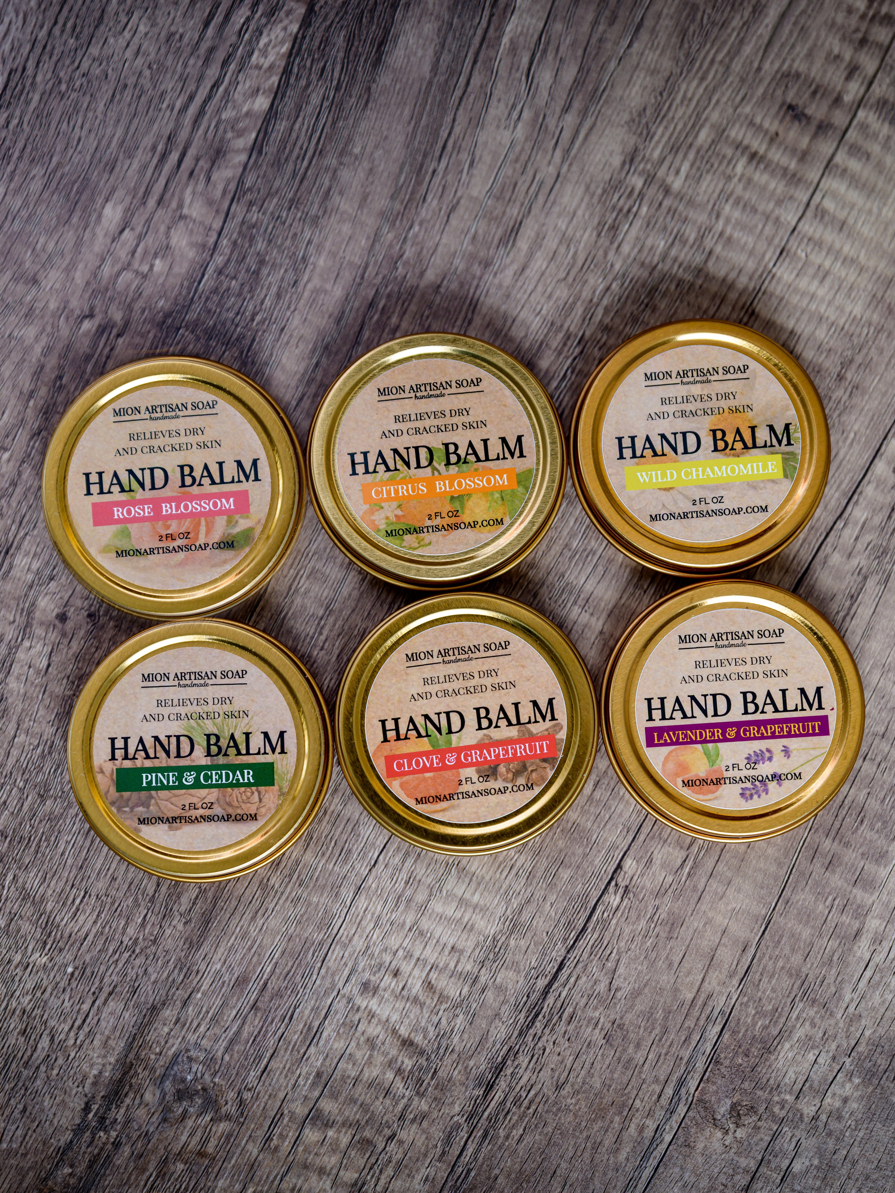 Six tins of hand balm with gold lids on a wooden surface